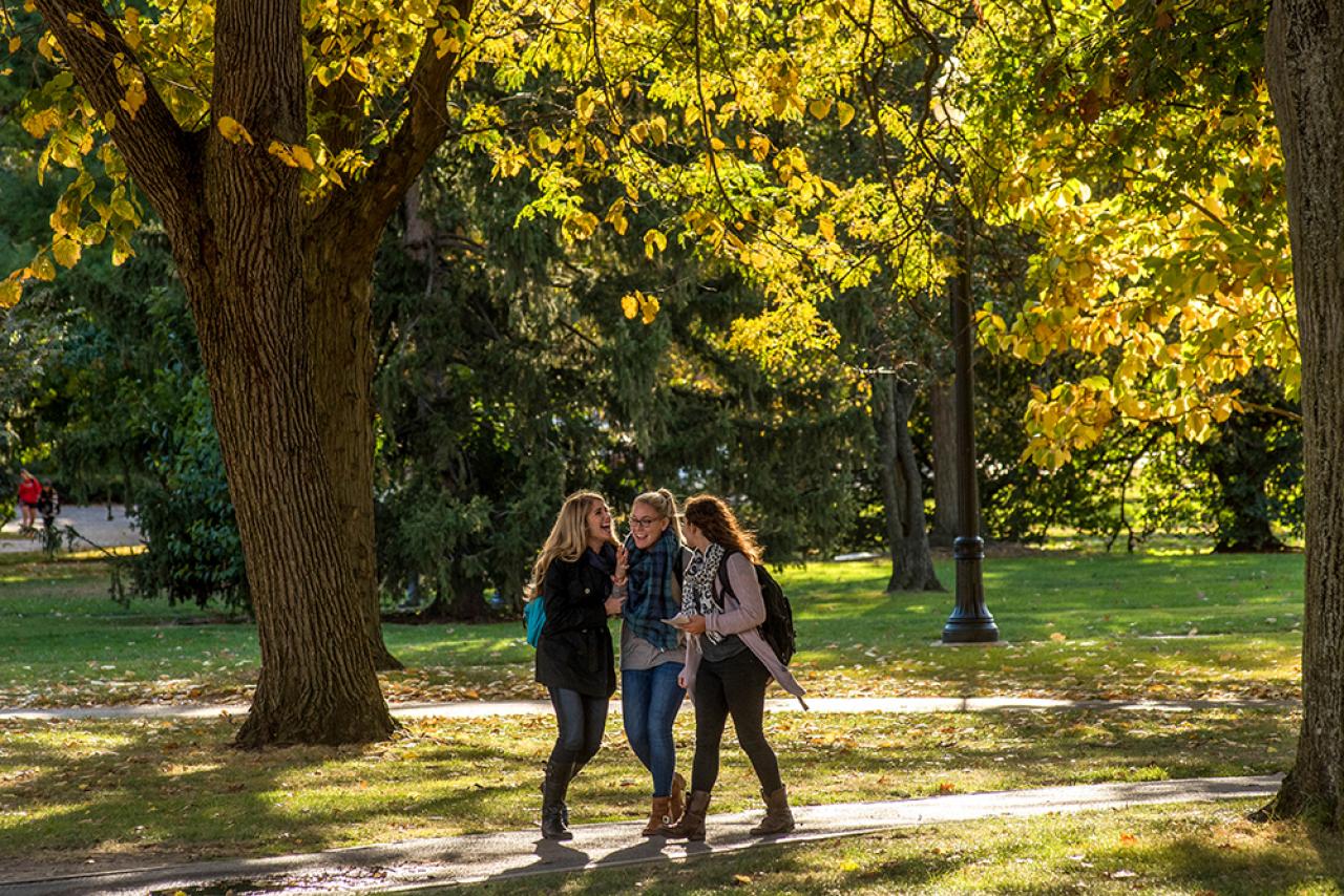Three girls walking and laughing on the oval in autumn